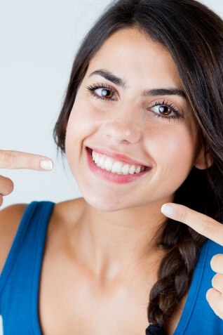 Woman with straight white teeth pointing to her smile